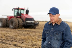 A royalty free image from the farming industry of a discouraged farmer in a field in front of a tractor.